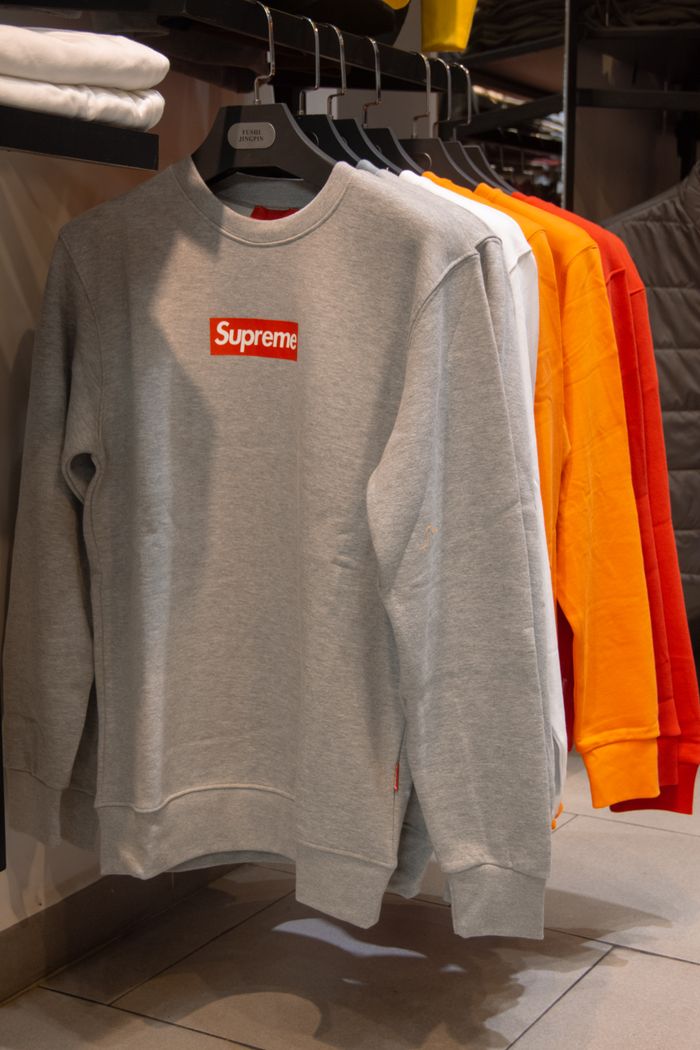 Mastering the First Impression: Your intriguing post title goes here A selection of Supreme sweaters in various colors displayed on hangers inside a trendy clothing store.